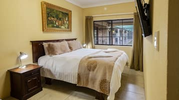 A neatly arranged bedroom with a bed, bedside table, lamp, and a large window with curtains.