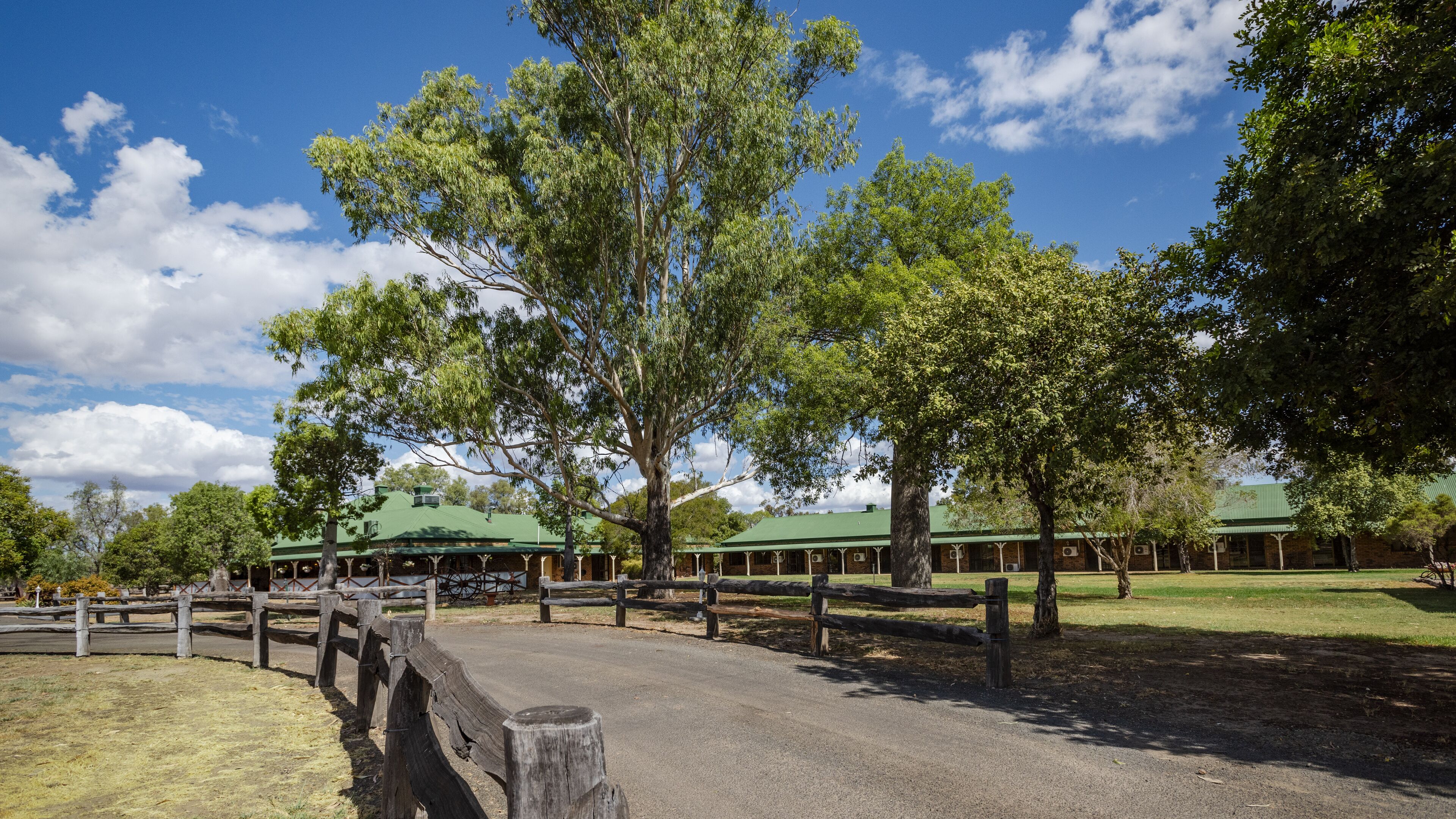 A large building with a green roof, surrounded by trees and a wooden fence.