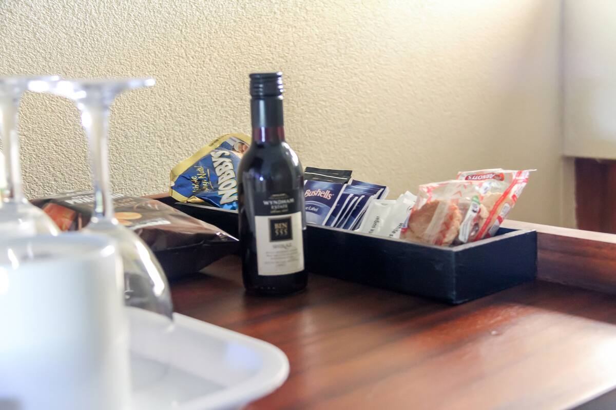 A bottle of wine, a glass, and a box of snacks on a wooden table.