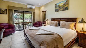 Een hotelkamer met een groot bed, een rode fauteuil, een kleine tafel en een balkon met uitzicht.
