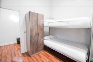 Una cama litera con un armario de madera en una habitación con suelo de madera y paredes blancas.