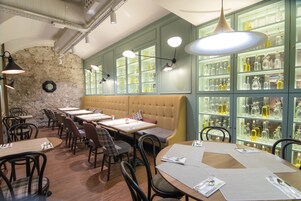 A restaurant with a stone wall, green cabinets, and a long bench. Tables are set with menus and cutlery.