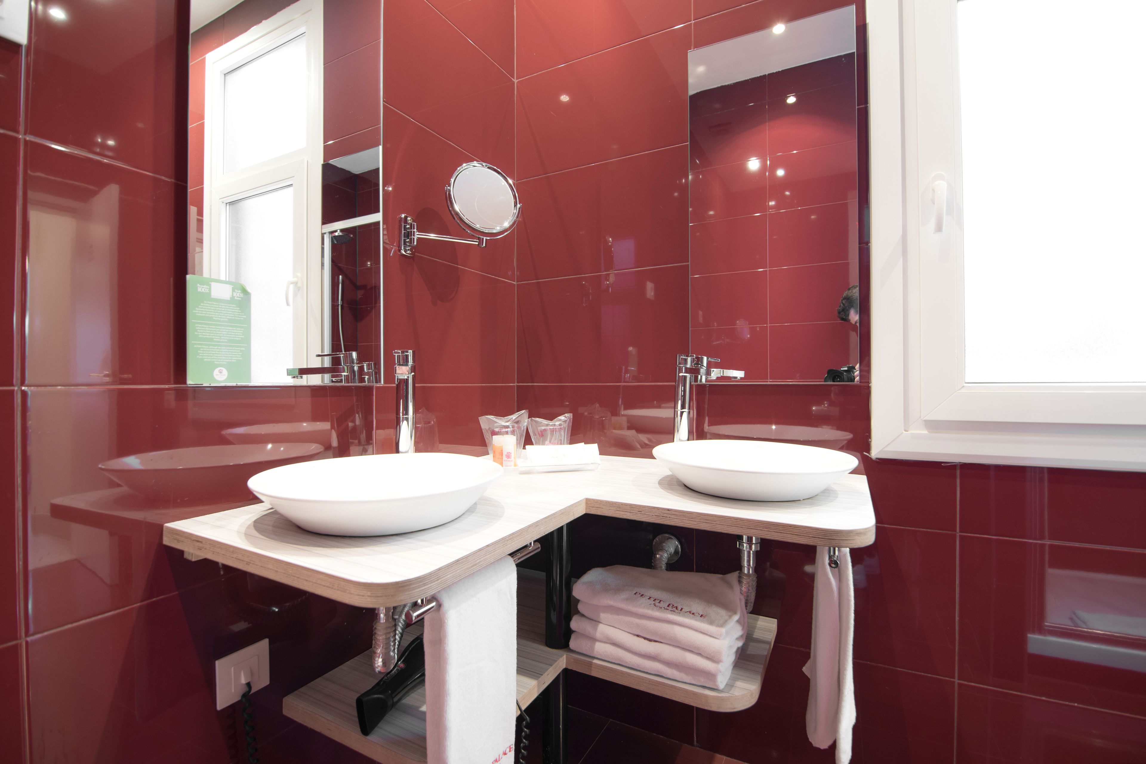 A modern bathroom with two white sinks, a mirror, and a red-tiled wall.