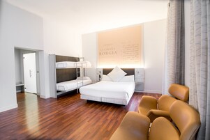 Ett hotellrum med en säng, två våningssängar, ett skrivbord, en stol och ett stort konstverk på väggen.