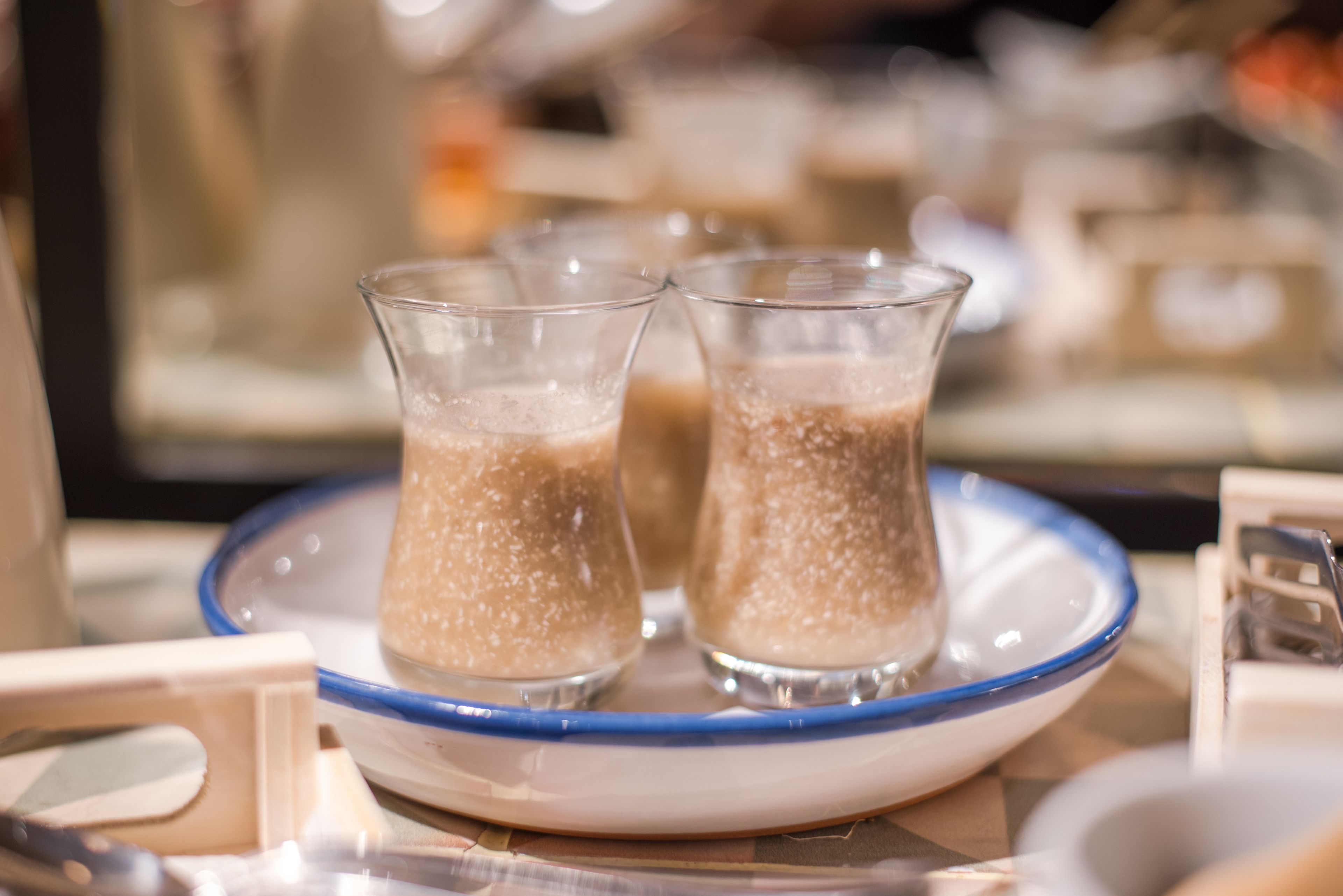 Three glasses of a beverage on a plate with a blue rim, placed on a table with a patterned tablecloth.