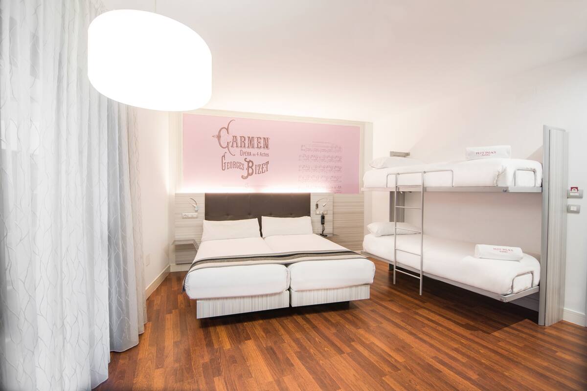 Un dormitorio moderno con una cama litera, una cama grande y una lámpara de pared.