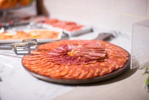 A round platter with sliced meats arranged in a circular pattern, accompanied by a knife and a fork on a table.