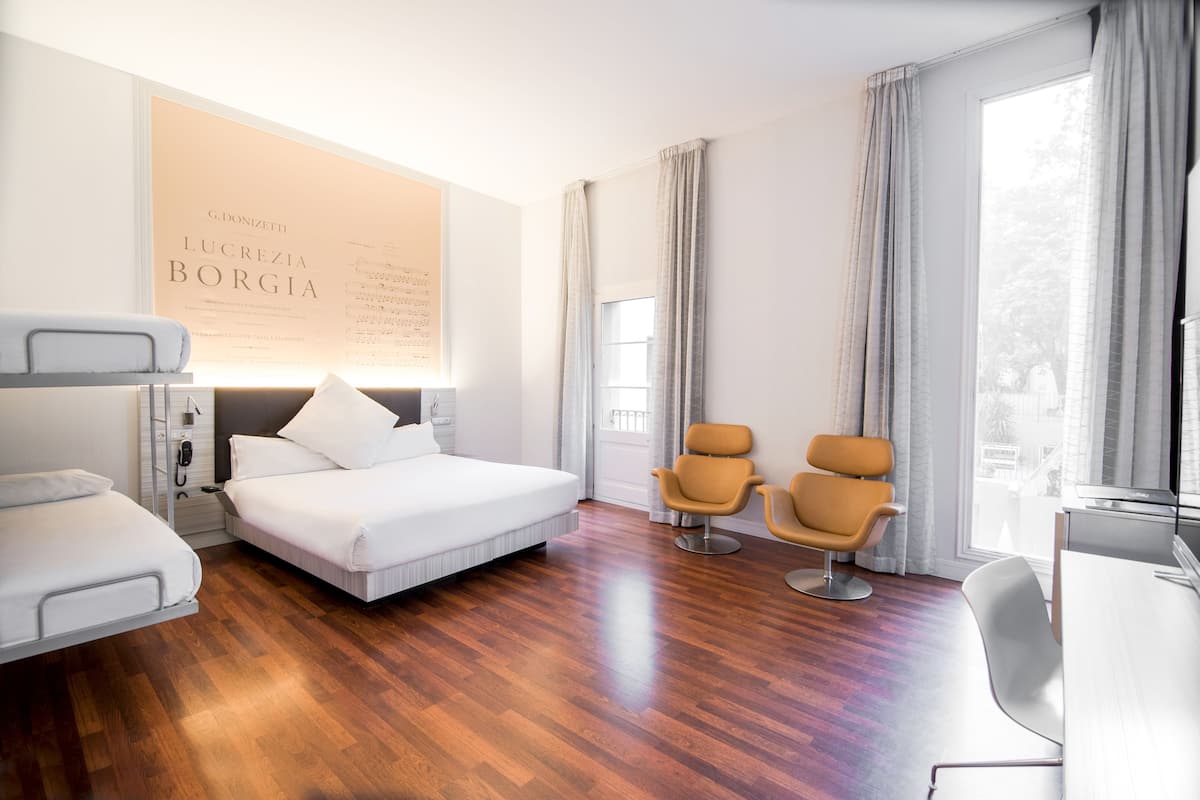 Una habitación de hotel moderna con una cama, dos sillones, un escritorio y un ventanal grande.