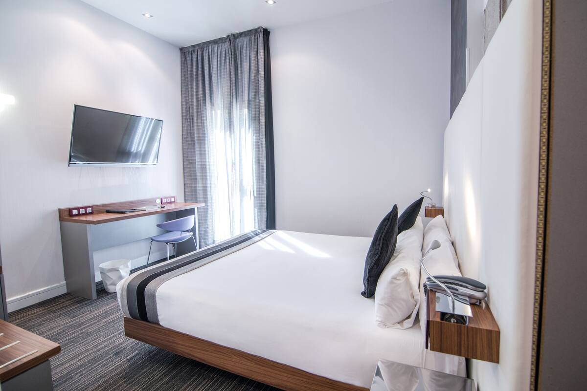 Una habitación de hotel moderna con una cama grande, un escritorio con televisor de pantalla plana y una ventana con cortinas.