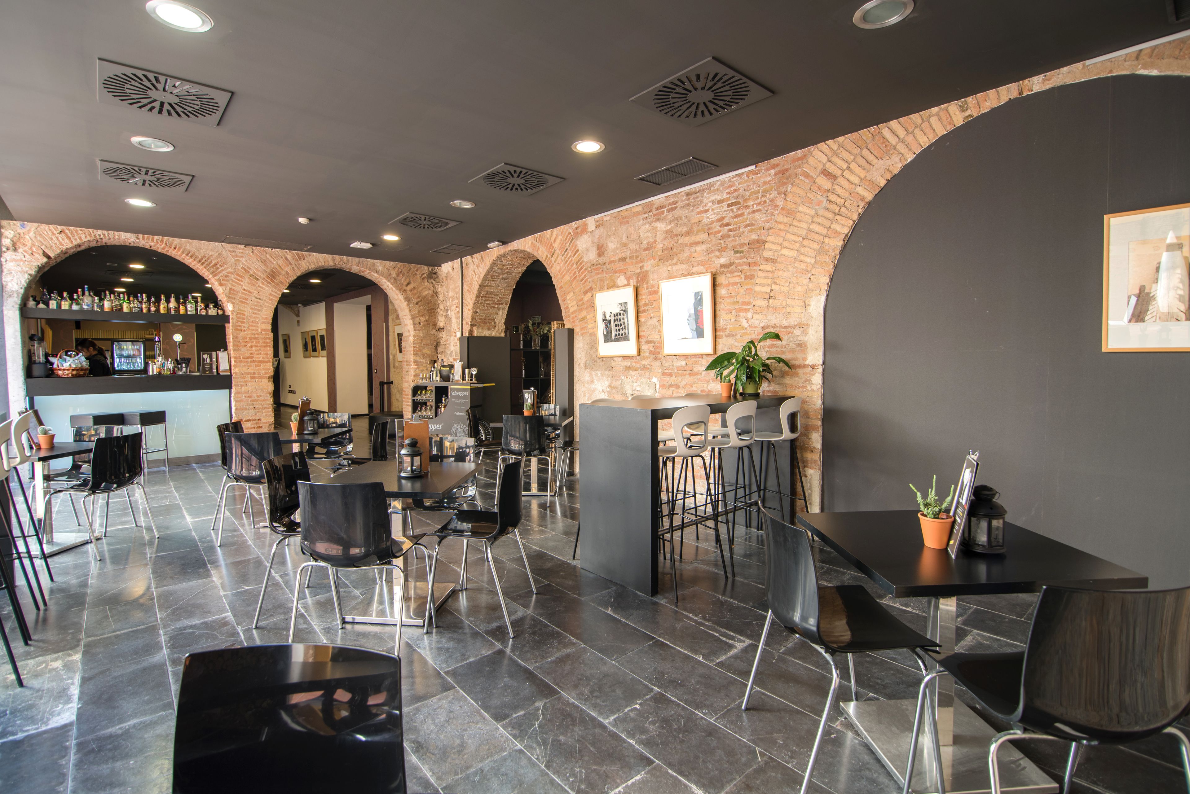 Un café moderno con arcos de ladrillo, sillas blancas y negras, y una zona de bar con estantes llenos de botellas.