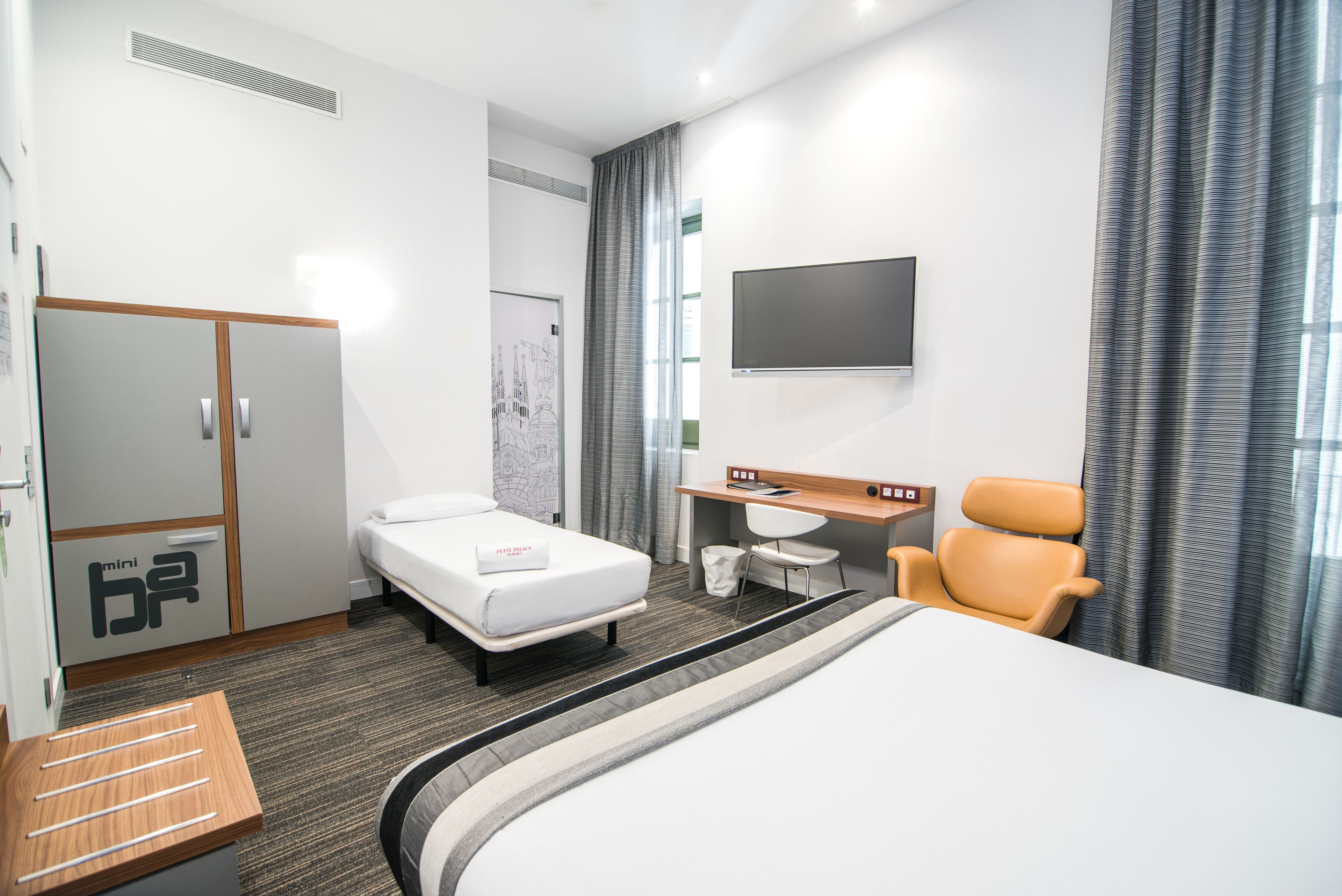 A hotel room with a bed, a desk, a chair, a TV, and a wardrobe.