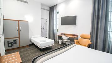 Habitació d'hotel amb un llit, una taula, una cadira, un televisor i un armari.