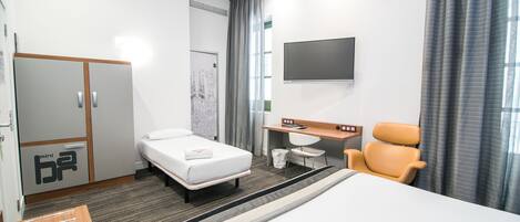 A hotel room with a bed, a desk, a chair, a TV, and a wardrobe.