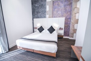 A modern hotel room with a large bed, a wooden headboard, and a stone accent wall.
