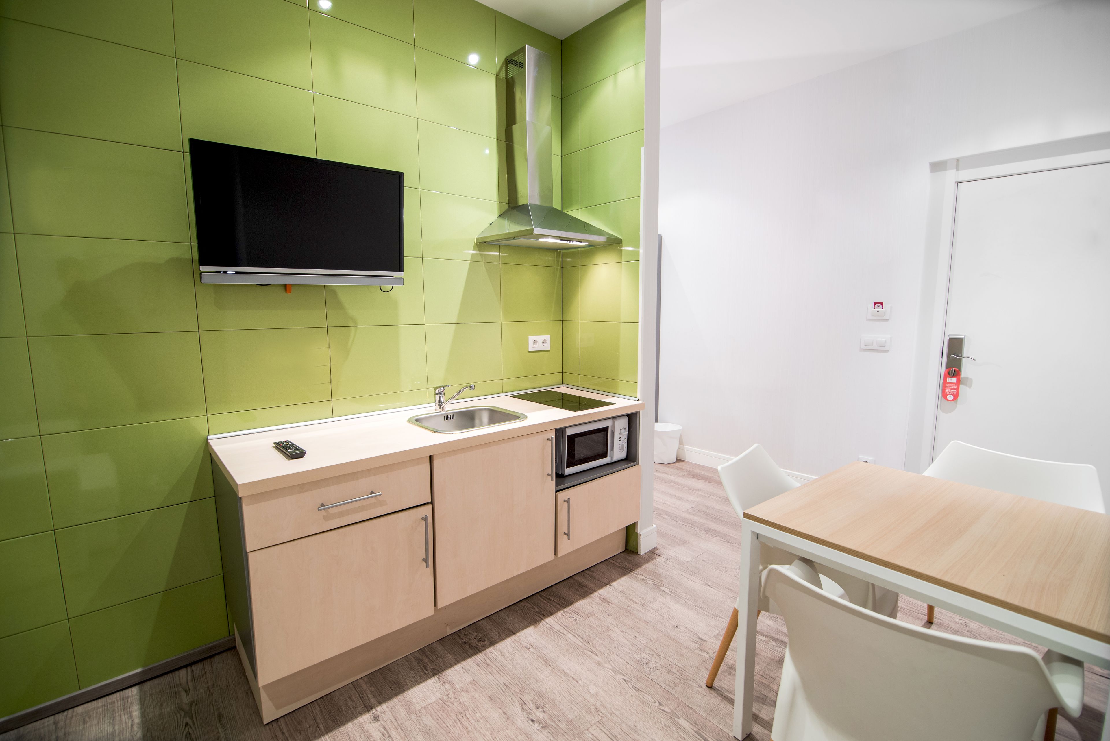 A modern kitchen with green walls, a flat-screen TV, stainless steel appliances, and a wooden dining table.