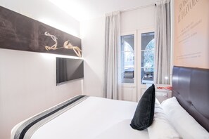 Une chambre d’hôtel avec un lit, un téléviseur à écran plat fixé au mur et une fenêtre avec des rideaux.