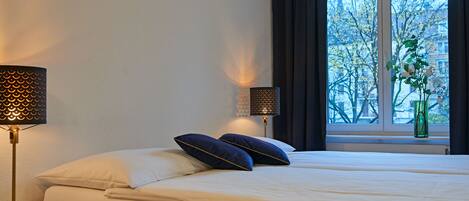 A neatly made bed with two pillows, a bedside lamp, and a nightstand with a drawer.