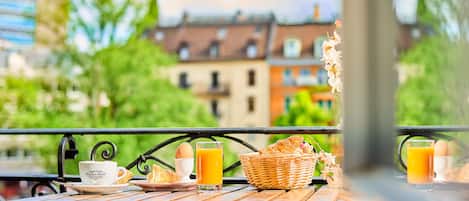 A wooden table with breakfast items including croissants, eggs, and orange juice, set against a cityscape view.