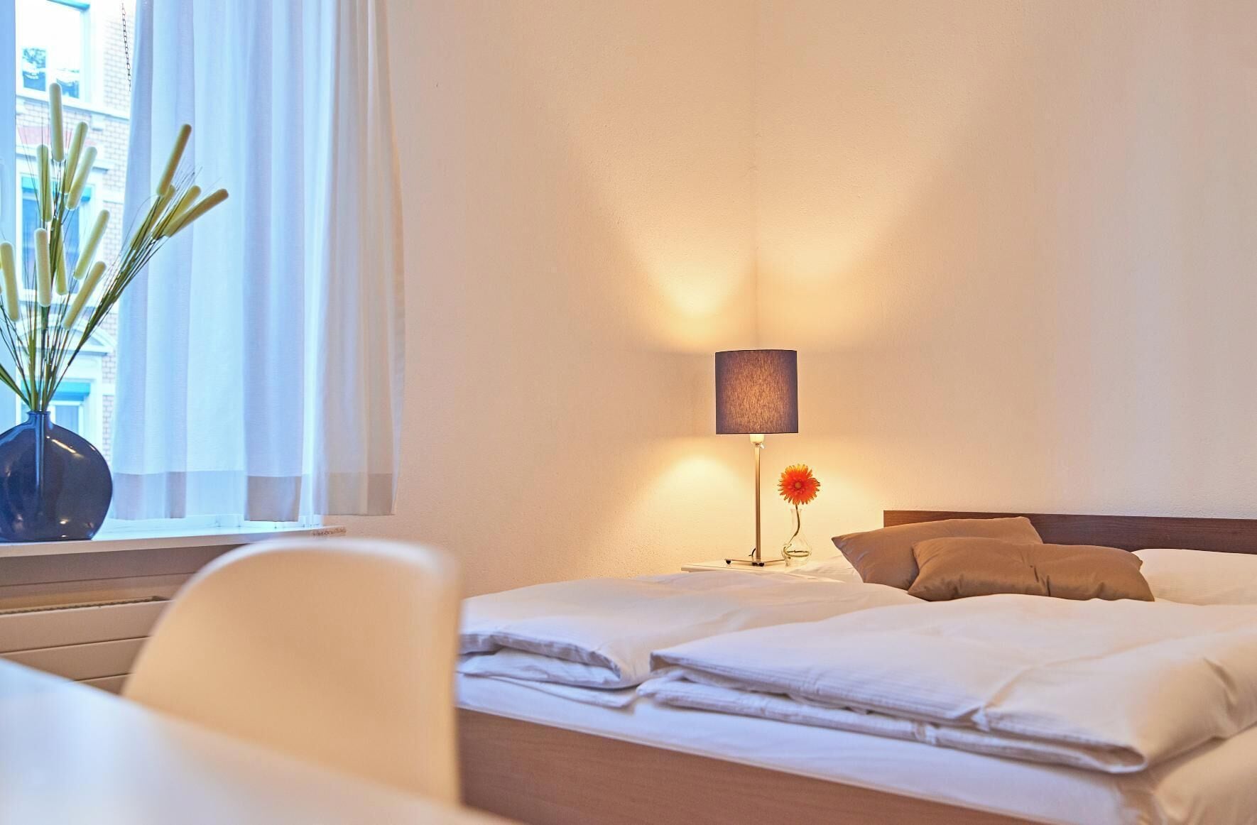 Une chambre d’hôtel avec un lit, une table de chevet, une lampe et une fenêtre avec des rideaux.
