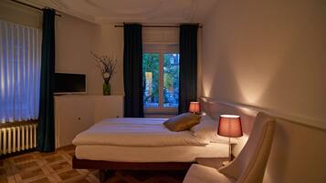 Une chambre d’hôtel avec un lit, deux lampes de chevet, une télévision, une fenêtre avec des rideaux et une vue sur l’extérieur.