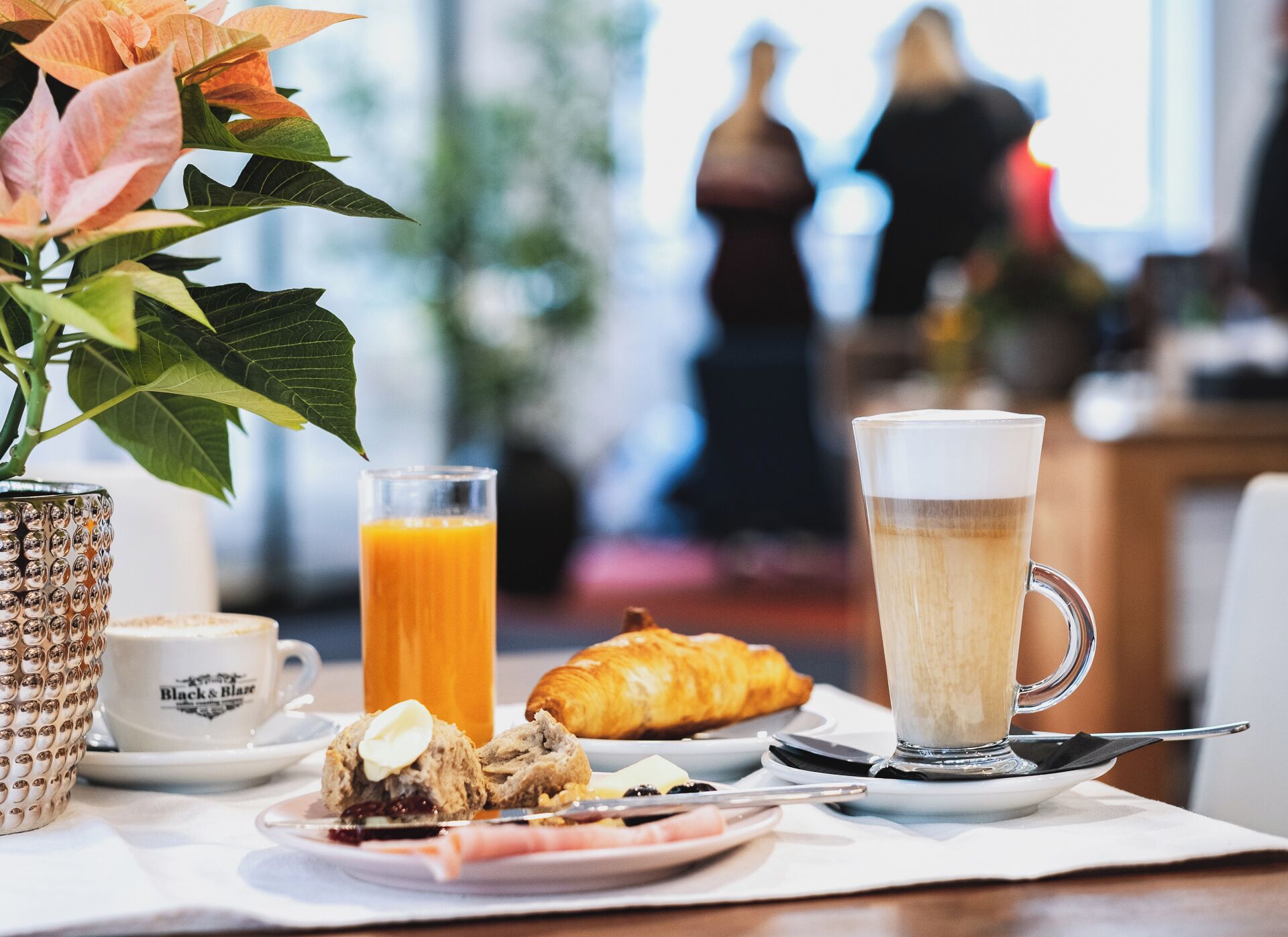 En frukostuppläggning med en croissant, kaffe, juice och ett bakverk på ett bord.