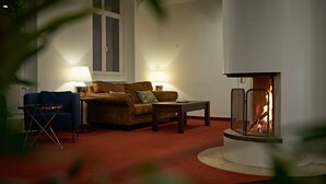 A cozy living room with a fireplace, a sofa, a coffee table, and a blue armchair. - Saint Georges Hotel (Zürich)