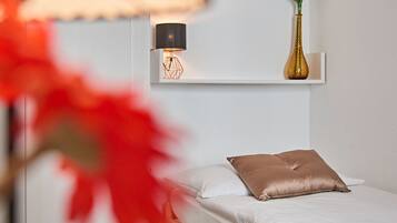A minimalist bedroom with a wooden bed, a bedside table with a lamp, and a potted plant on a shelf.