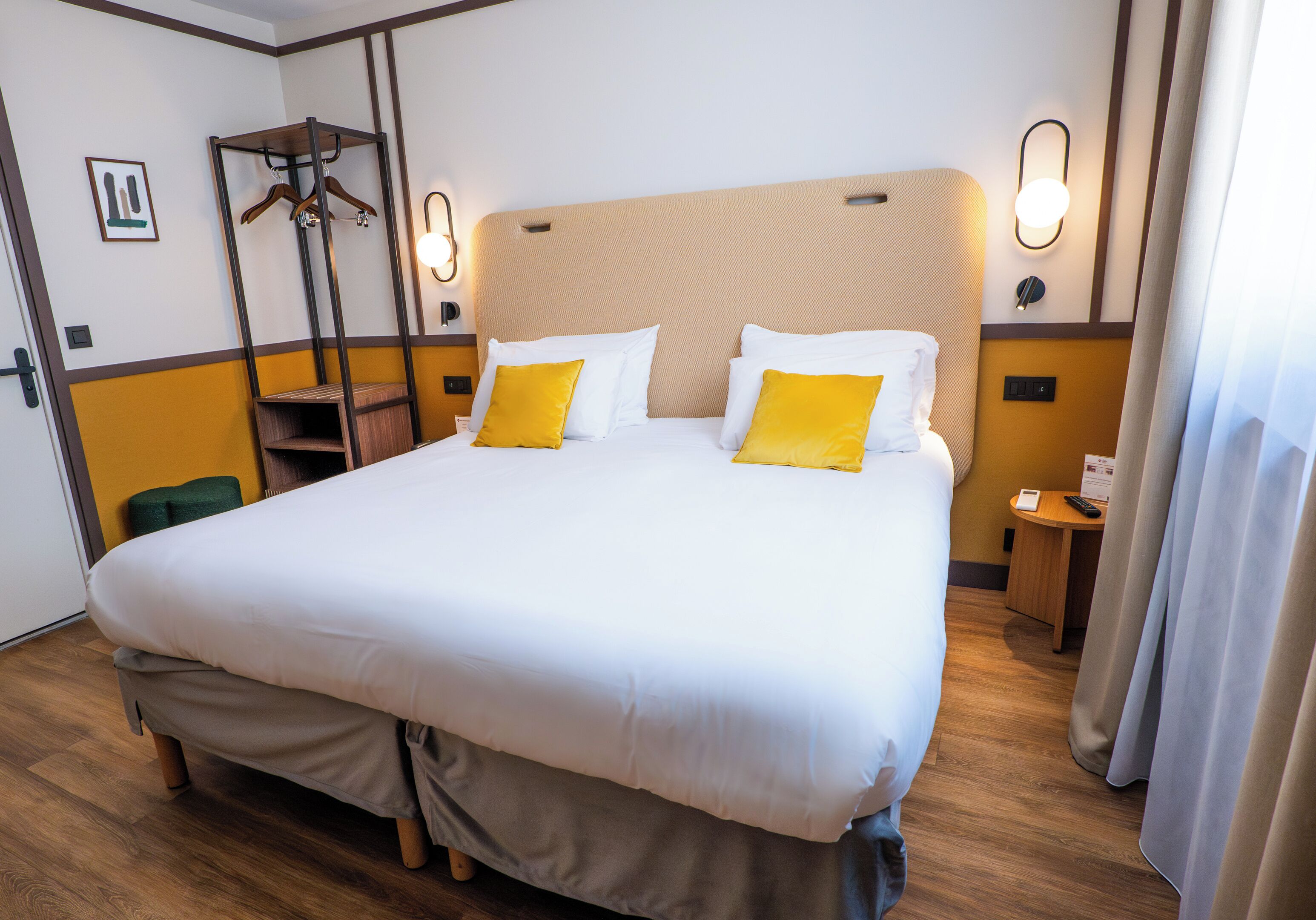 Una habitación de hotel con una cama grande, una mesita de noche, un perchero y una lámpara de pared.