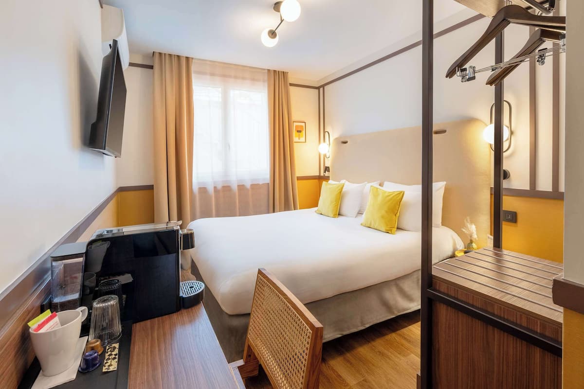 Une chambre d’hôtel avec un lit, un bureau doté d’une machine à café, une télévision et une fenêtre avec des rideaux.