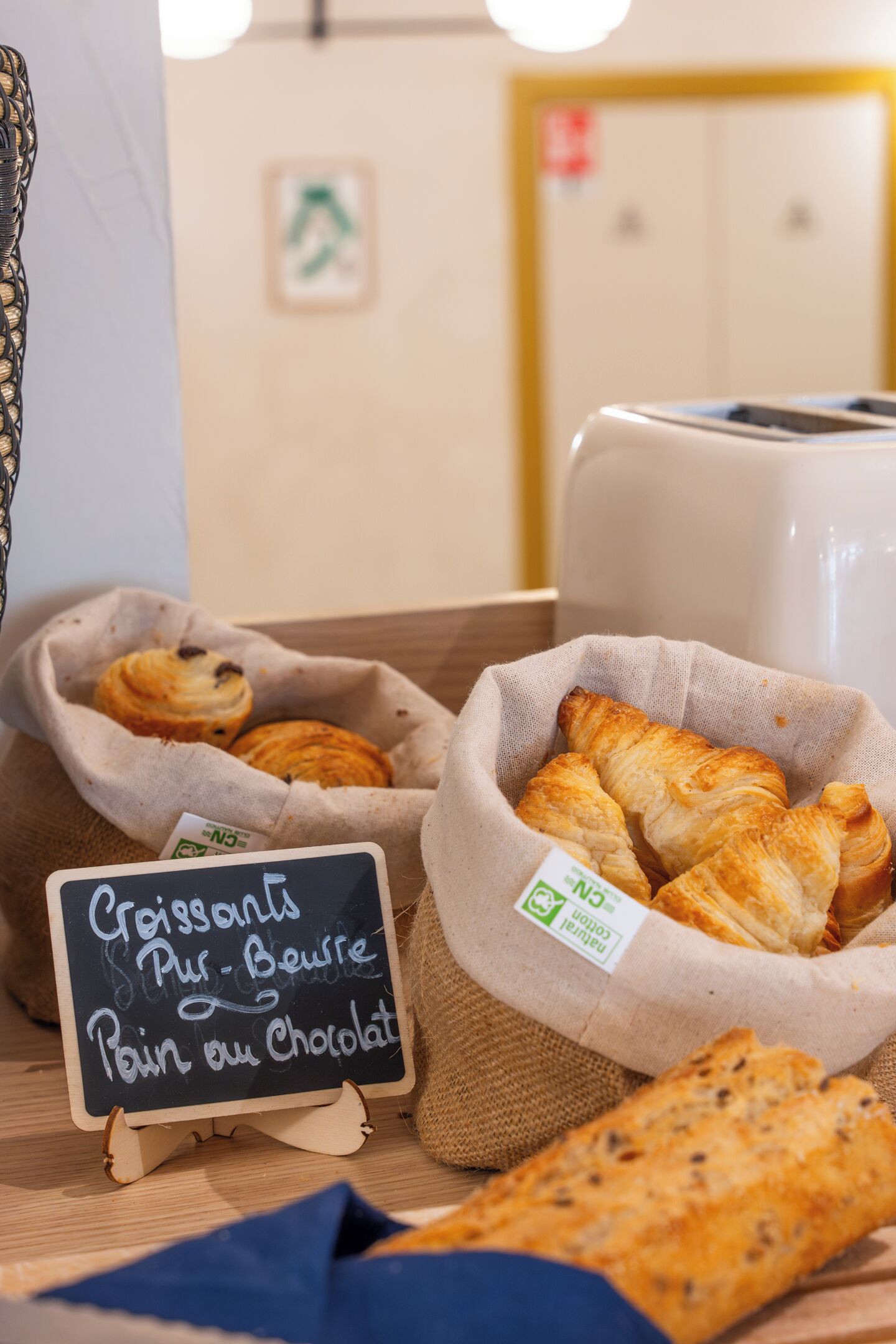 A bakery display with pastries in burlap bags and a chalkboard sign.