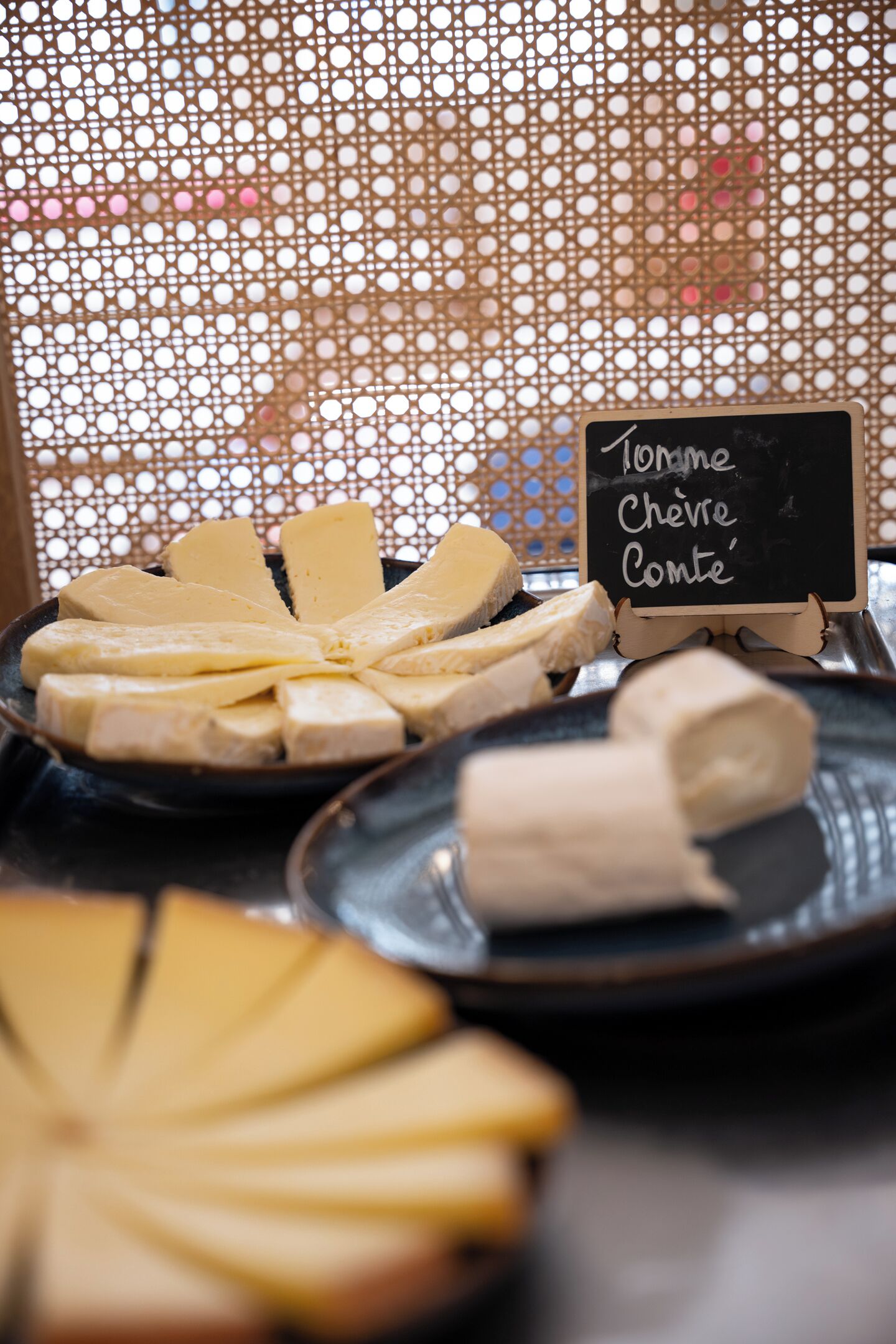 Une sélection de fromages présentés sur des assiettes, avec une étiquette indiquant « Tomme de chèvre du Comte ».