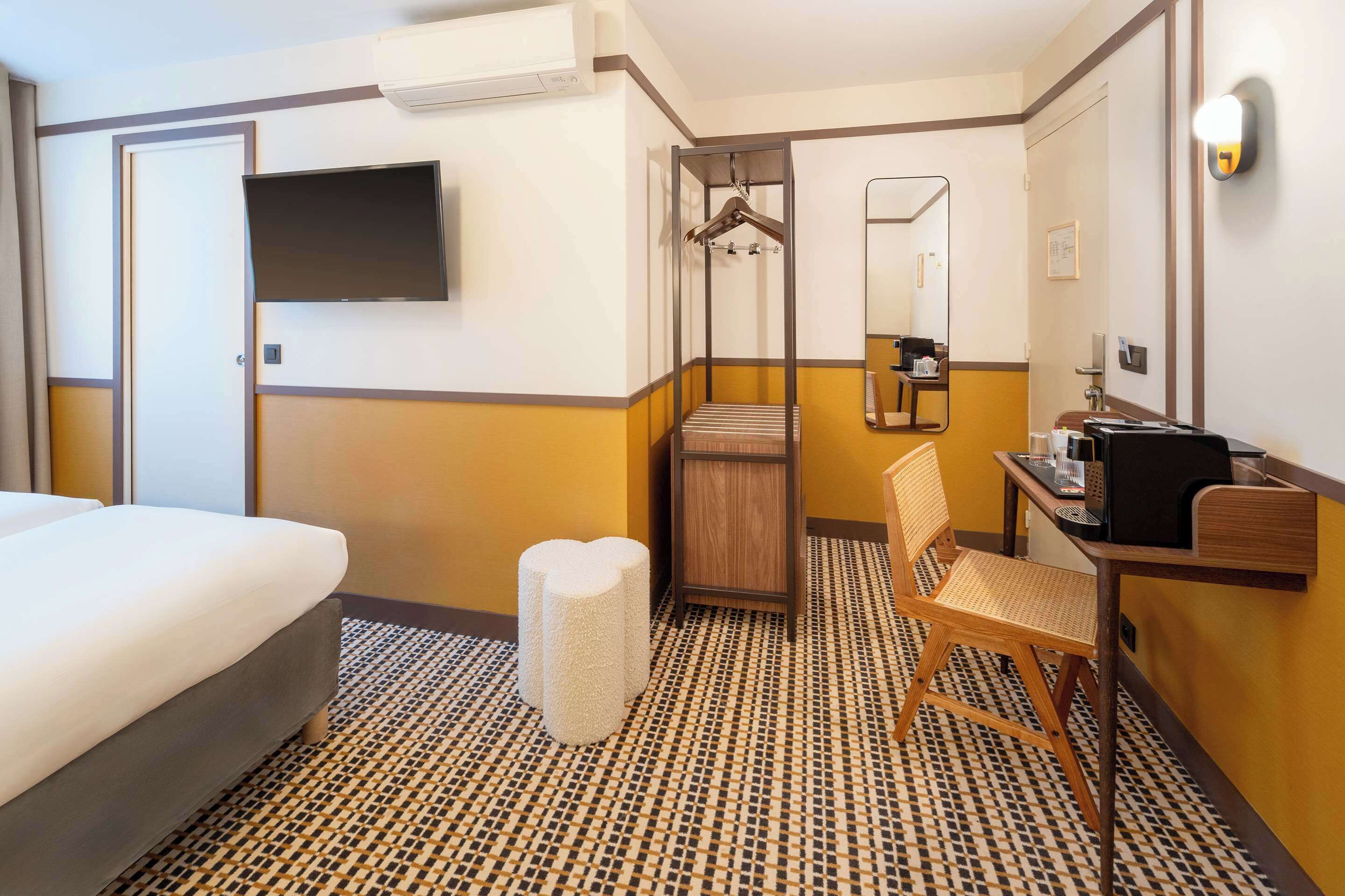 Une chambre d’hôtel comprenant un lit, un bureau avec une chaise, un miroir, une télévision et une salle de bain avec une douche et un porte-serviettes.