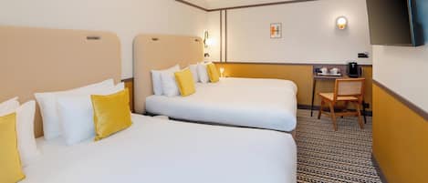 A hotel room with two beds, a desk, a chair, a TV, and a coffee machine.