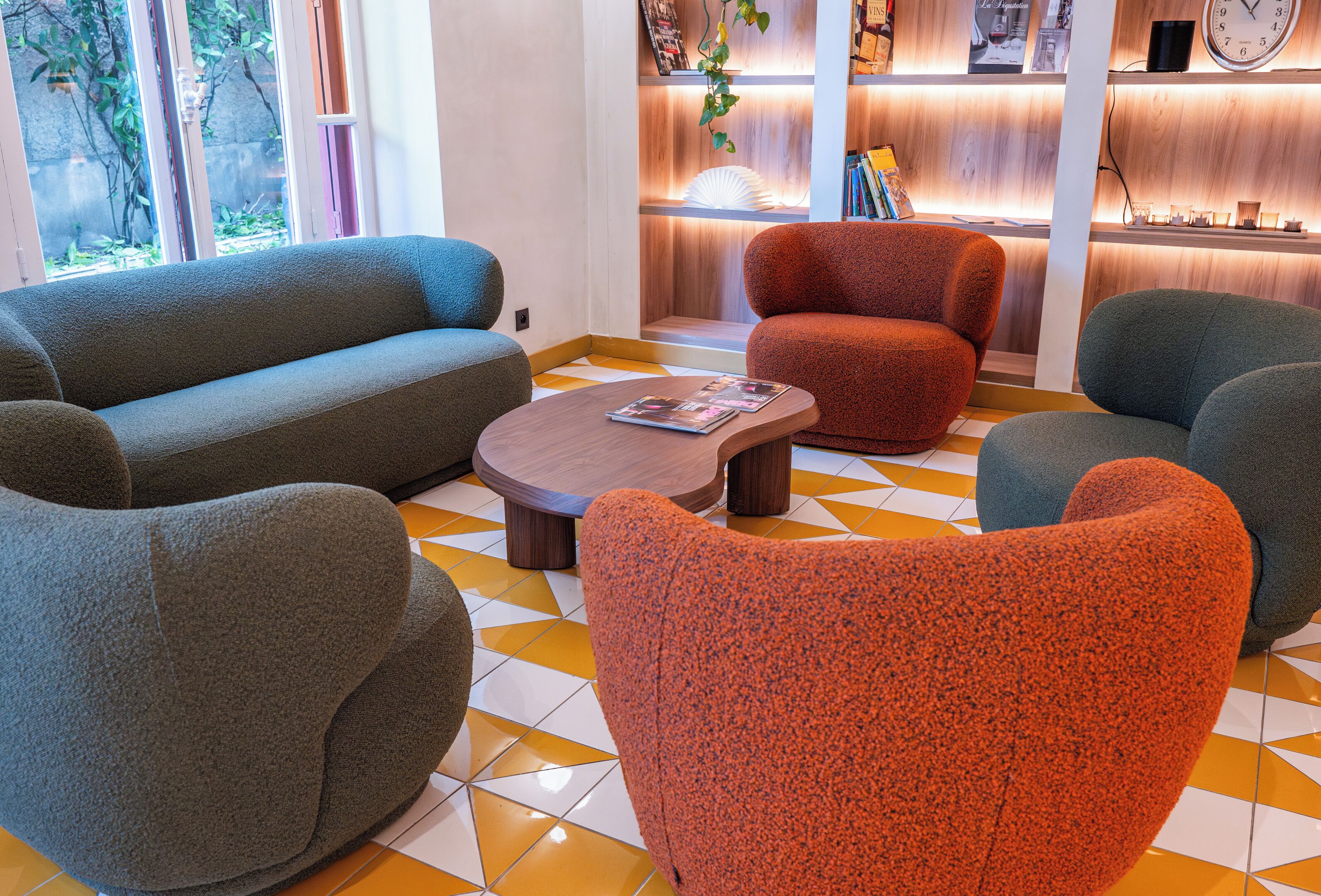 Een moderne zithoek met banken en fauteuils, een salontafel en een houten receptiebalie met boeken en een klok.