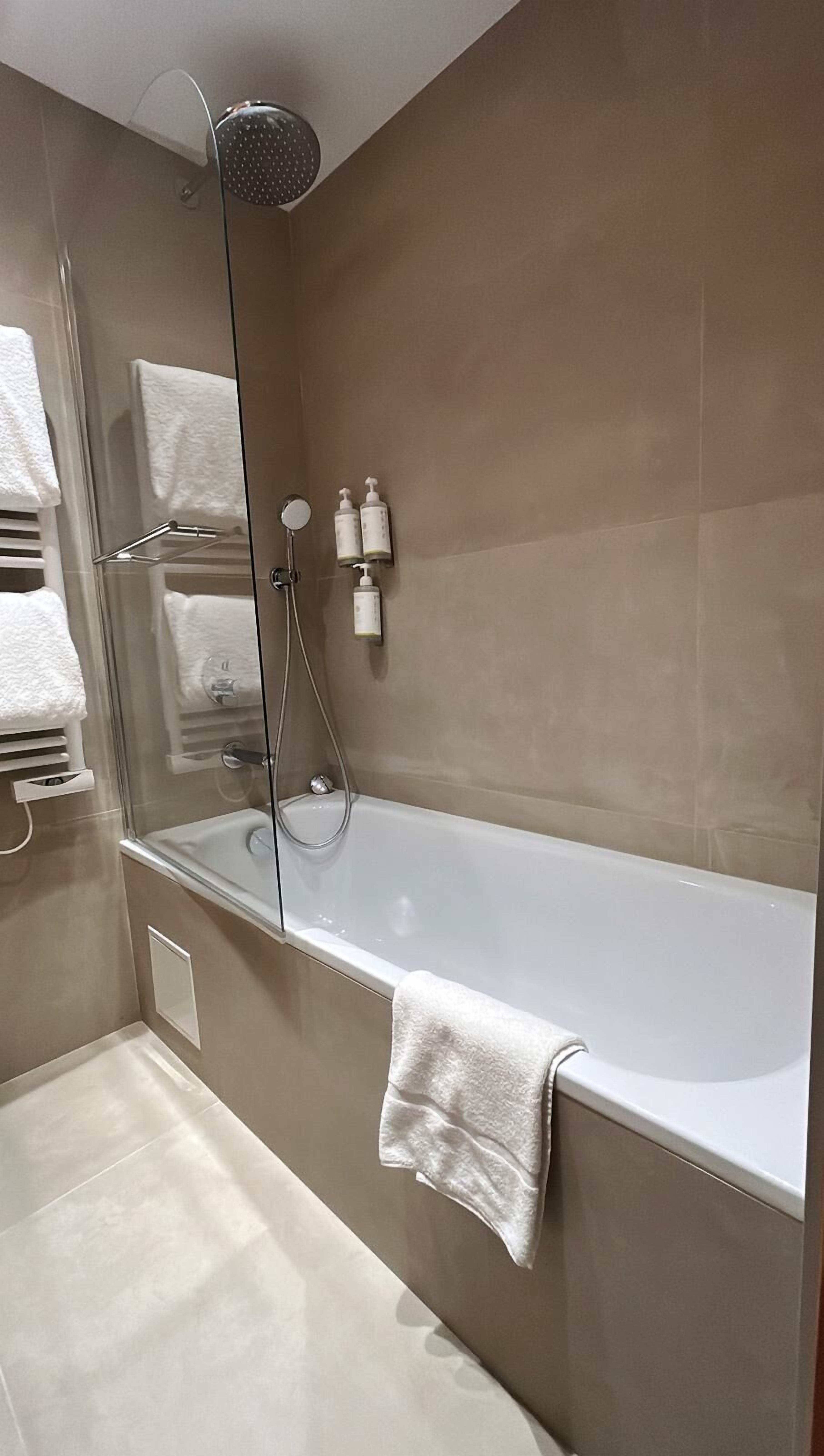 A modern bathroom with a glass-enclosed shower, a white bathtub, and a towel rack.