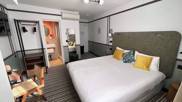 A hotel room with a large bed, a desk, a chair, a wardrobe, and a bathroom visible through an open door.