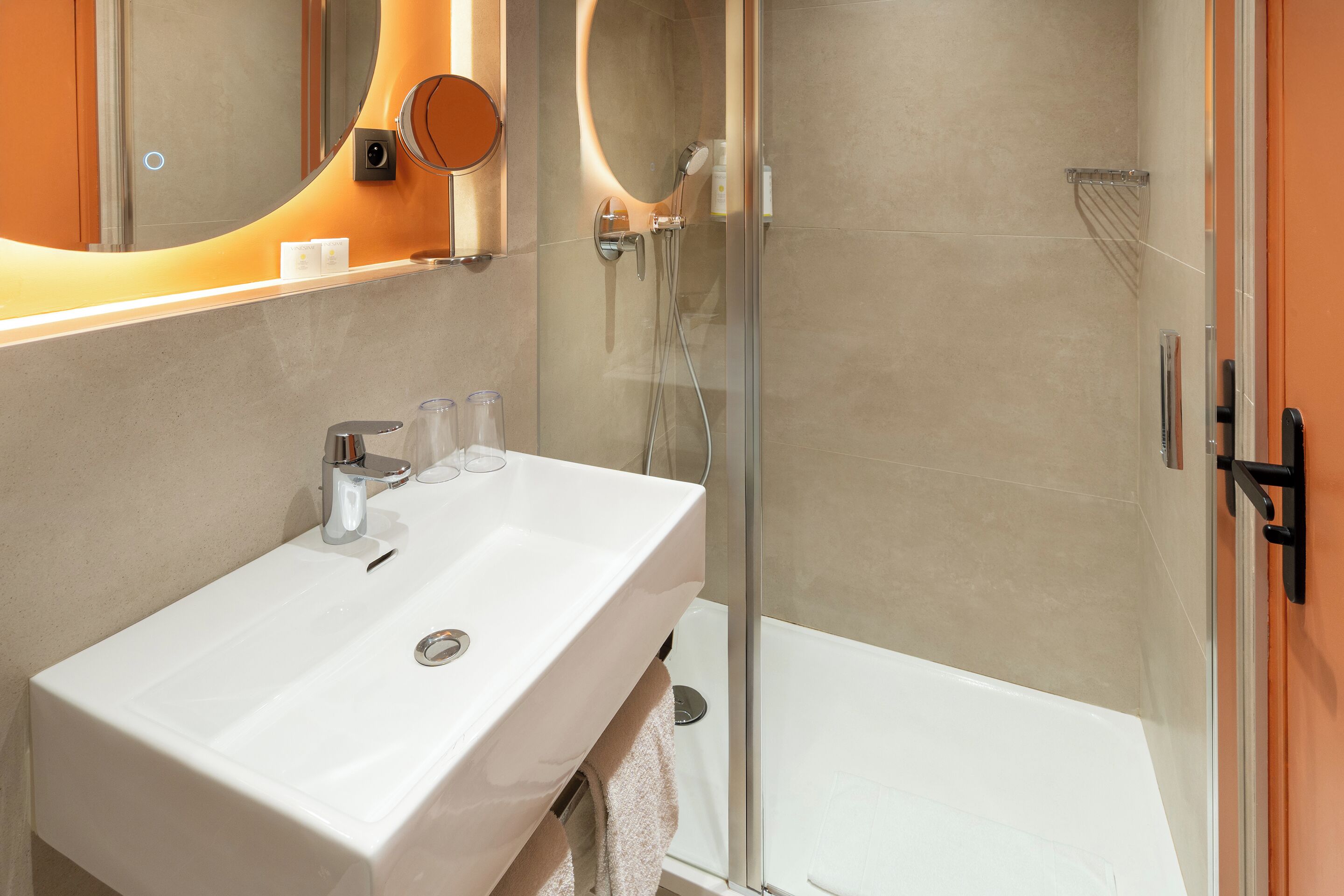 A modern bathroom with a white sink, a glass shower enclosure, and a mirror with a circular frame.