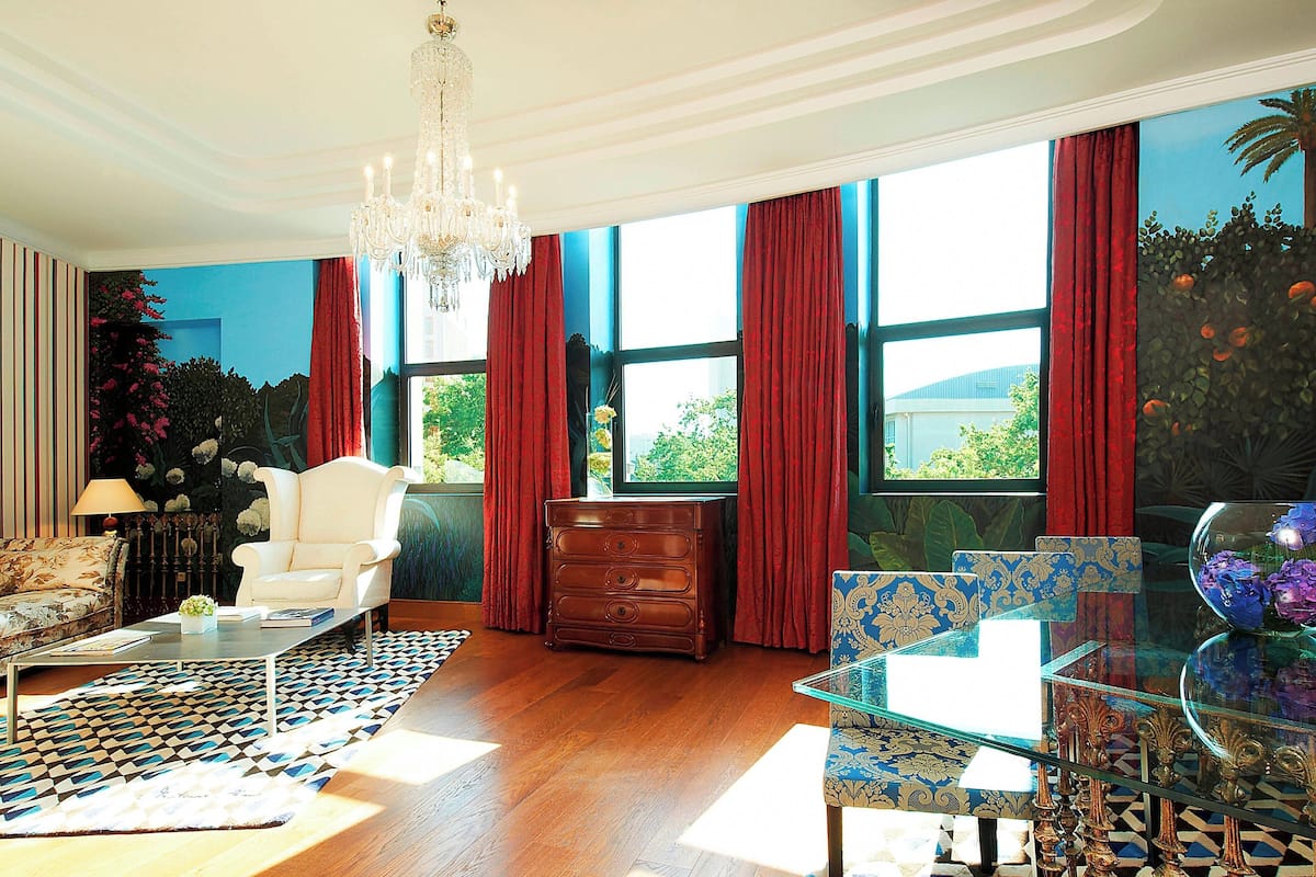 Un salón amplio con un ventanal grande, una araña, un sillón blanco, un aparador de madera y una mesa de centro de cristal.