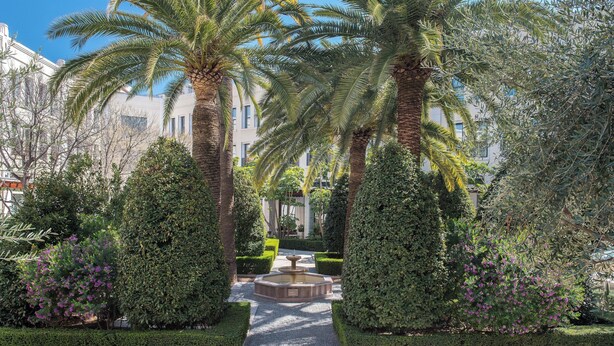 Un jardín bien cuidado con palmeras, una fuente central y setos podados.