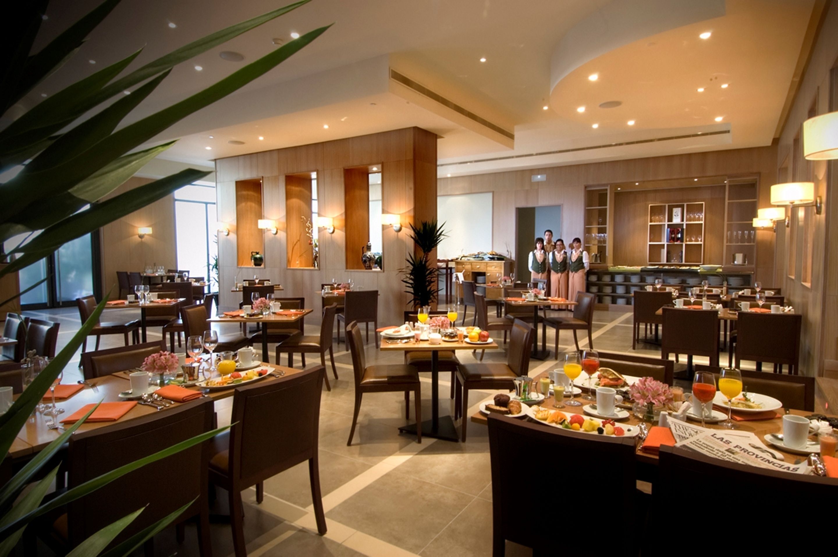 A spacious hotel dining area with multiple tables set for breakfast, featuring a variety of dishes and drinks.