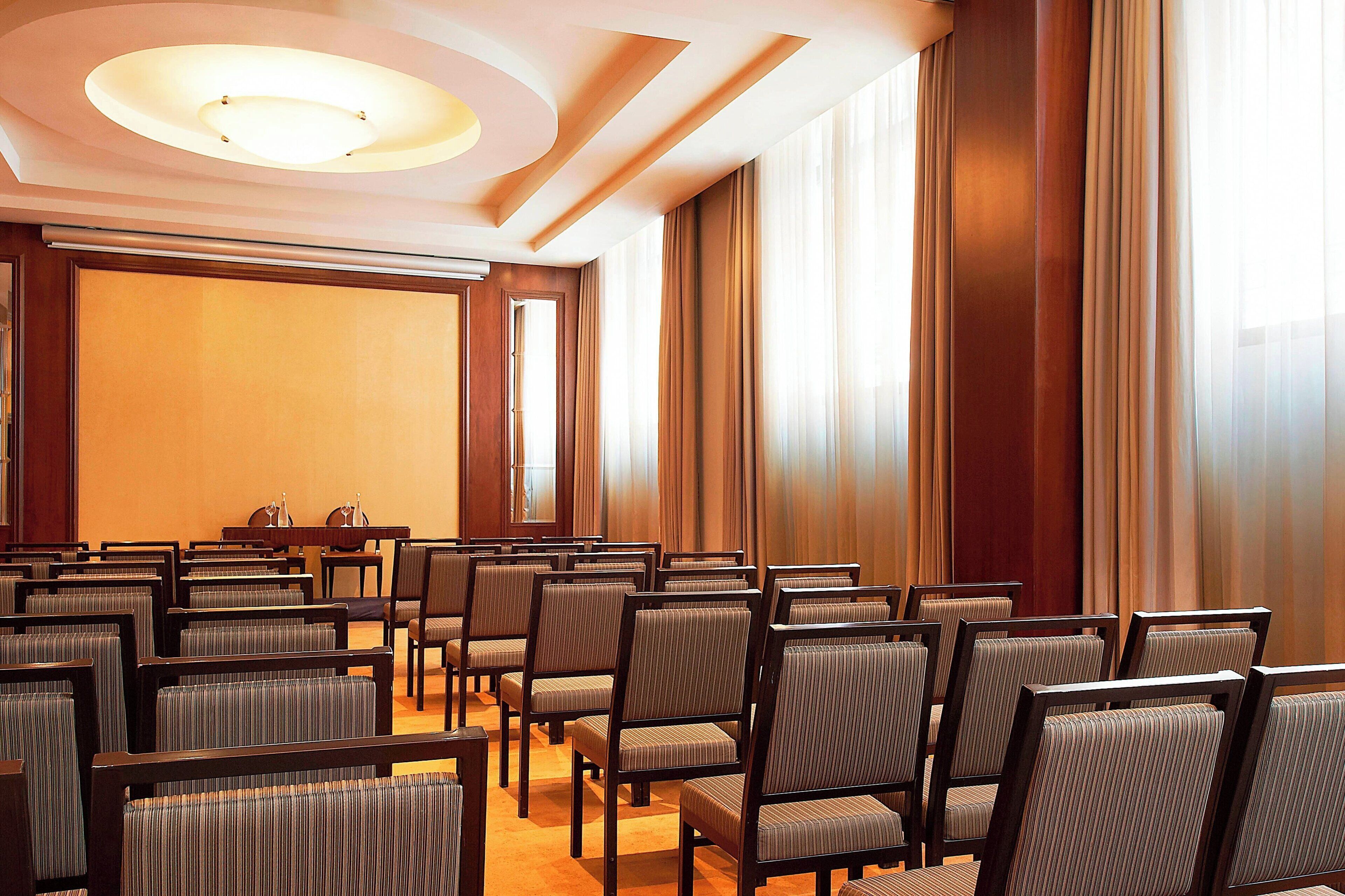 A conference room with rows of chairs, a podium, and a large screen.