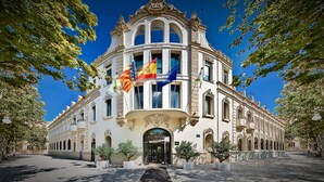 Un edificio histórico con una entrada imponente, varias banderas y arquitectura clásica.