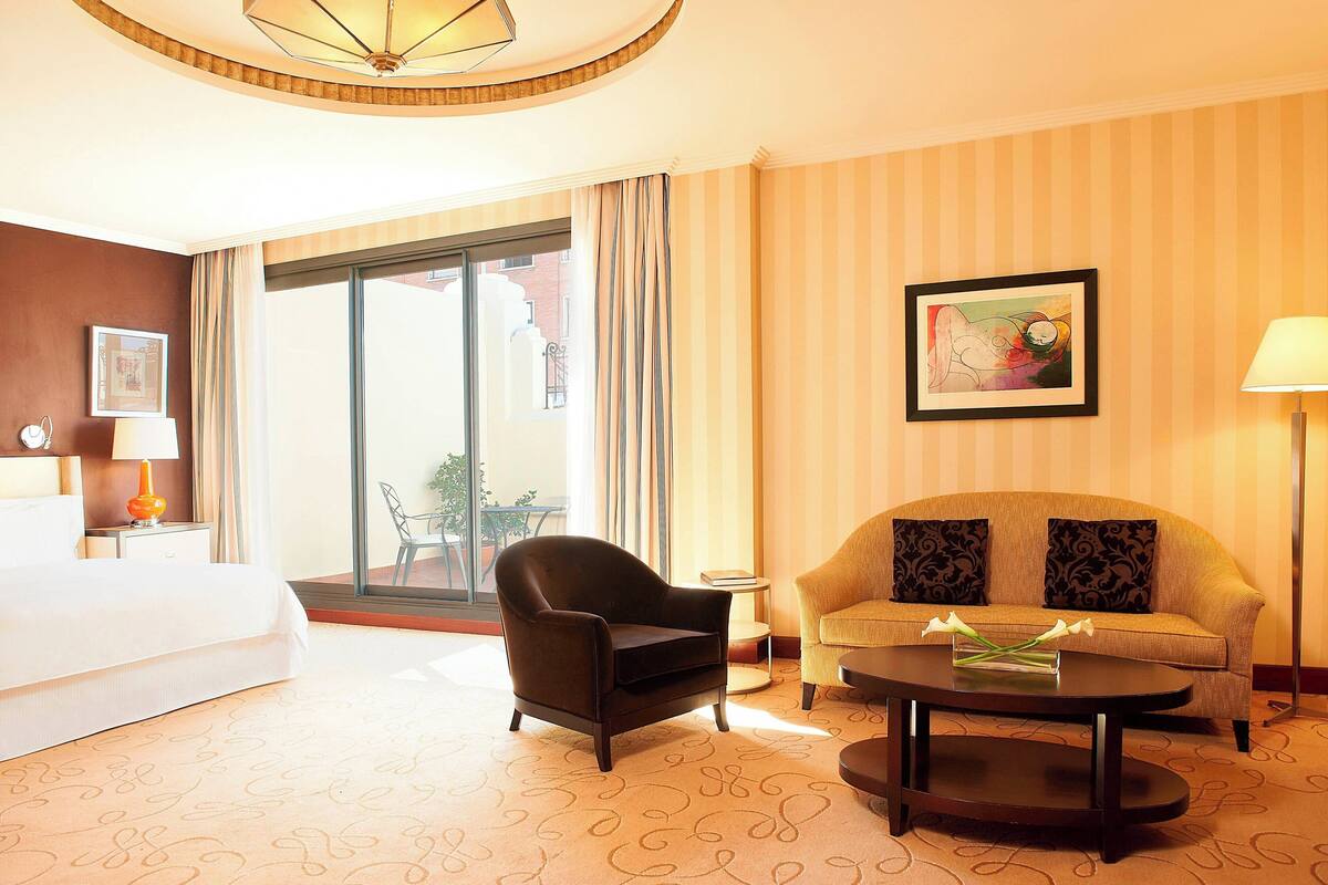 Una habitación de hotel con cama, sofá, sillón, mesita de centro y un cuadro en la pared.