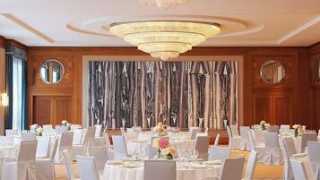 Un salón de banquetes con mesas redondas, sillas blancas y candelabros.