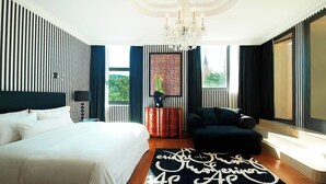 Un dormitorio moderno con una cama grande, un sofá oscuro, una araña y vistas a un edificio.