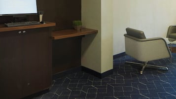 Zona de recepción con un mostrador, una computadora, una silla y un cartel en la pared.
