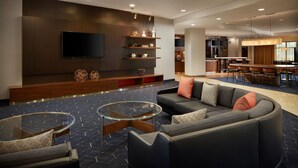 A modern hotel lobby with a curved sofa, a glass coffee table, and a flat-screen TV mounted on the wall. - Courtyard by Marriott Winchester (Winchester)