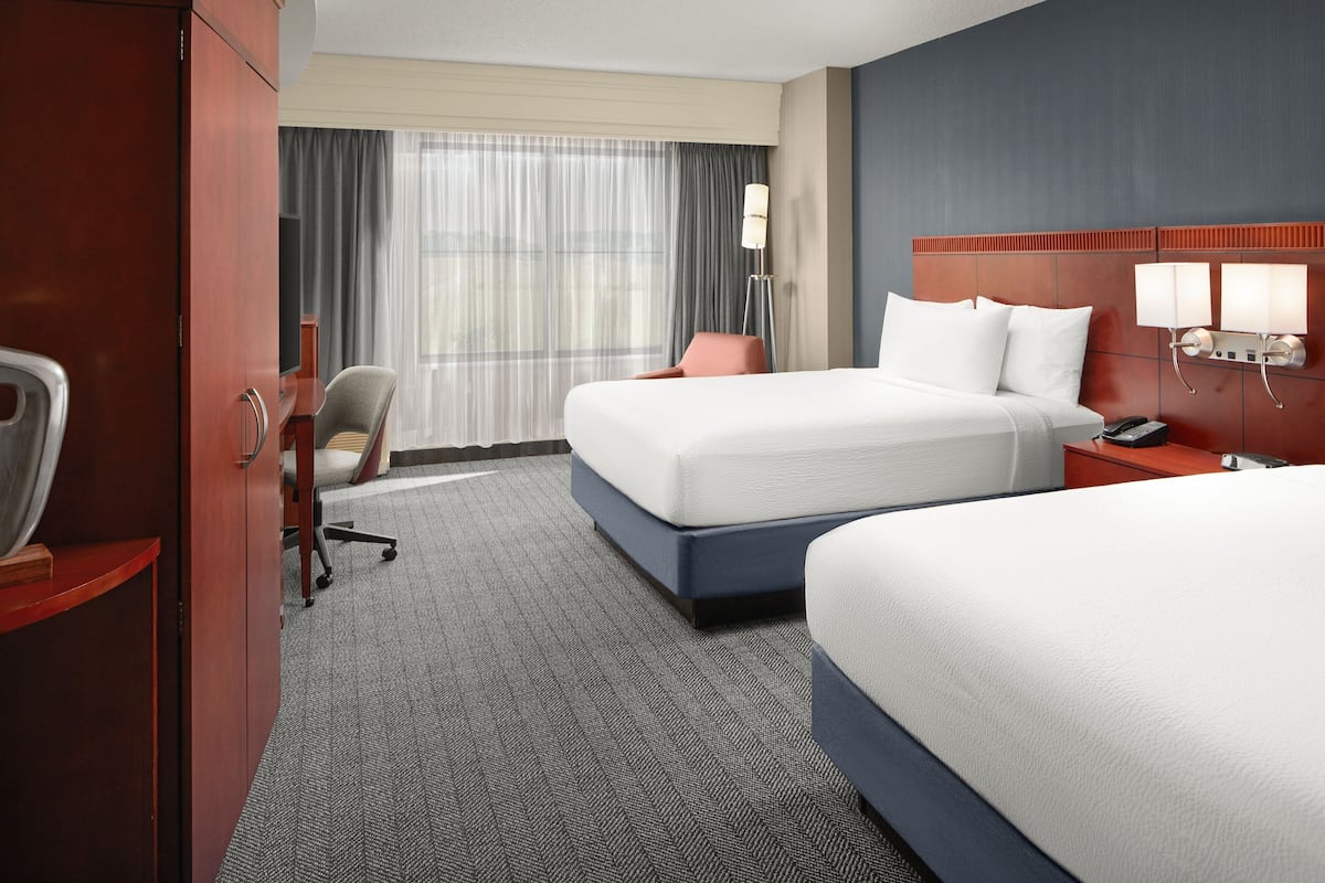 A hotel room with two beds, a desk, a chair, and a large window with curtains.