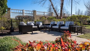 An outdoor seating area with wicker furniture and a small table, surrounded by greenery and a building in the background. - Courtyard by Marriott Winchester (Winchester)