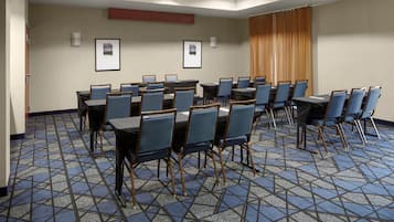 Un salón de conferencias con alfombra de diseño geométrico, sillas tapizadas en azul y mesas.
